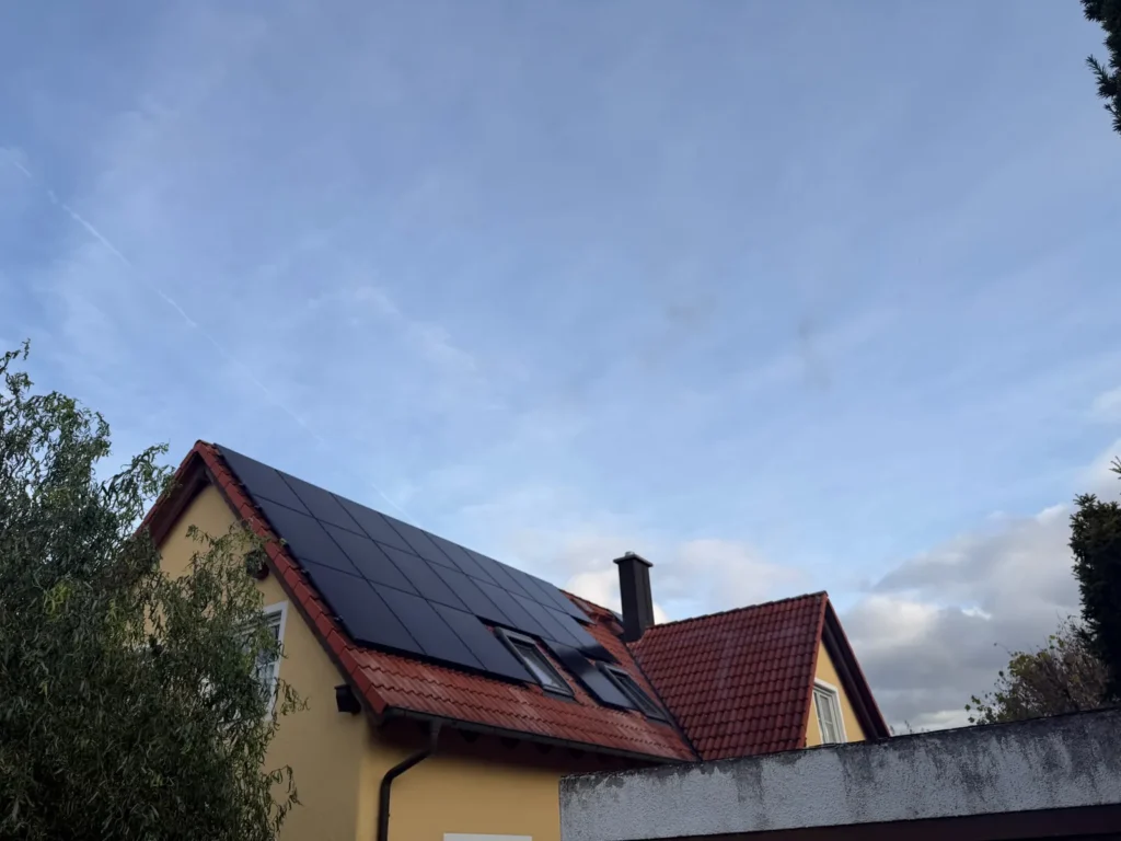 Wohnhaus mit schwarzen Solarmodulen auf dem roten Ziegeldach unter blauem Himmel