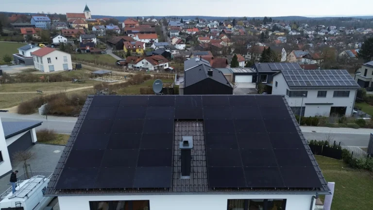 Luftaufnahme: Einfamilienhaus mit schwarzer Photovoltaikanlage, dahinter ein bayerischer Ort