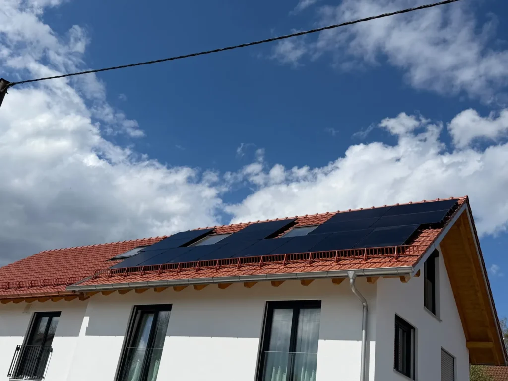Photovoltaikanlage mit schwarzen Modulen auf dem roten Ziegeldach eines Wohnhauses