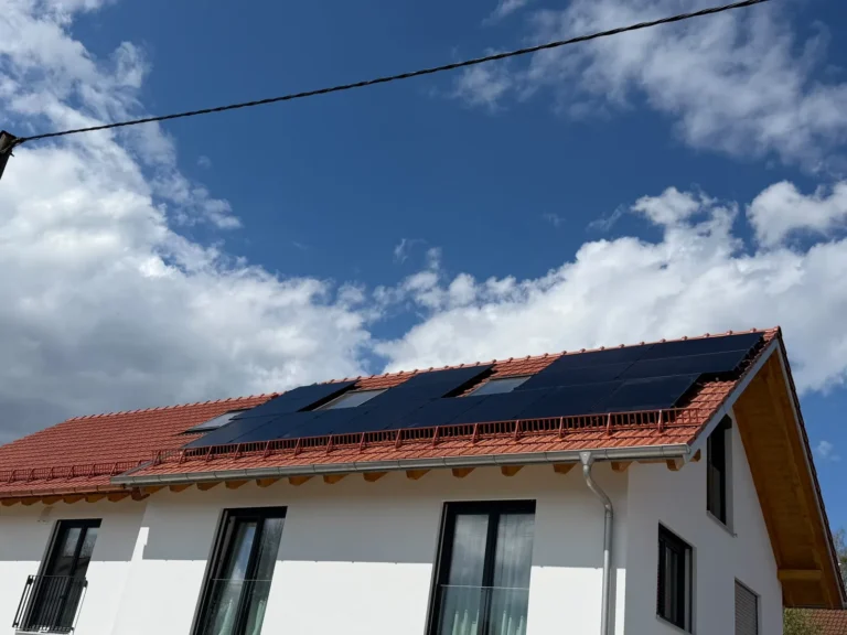 Photovoltaikanlage mit schwarzen Modulen auf dem roten Ziegeldach eines Wohnhauses