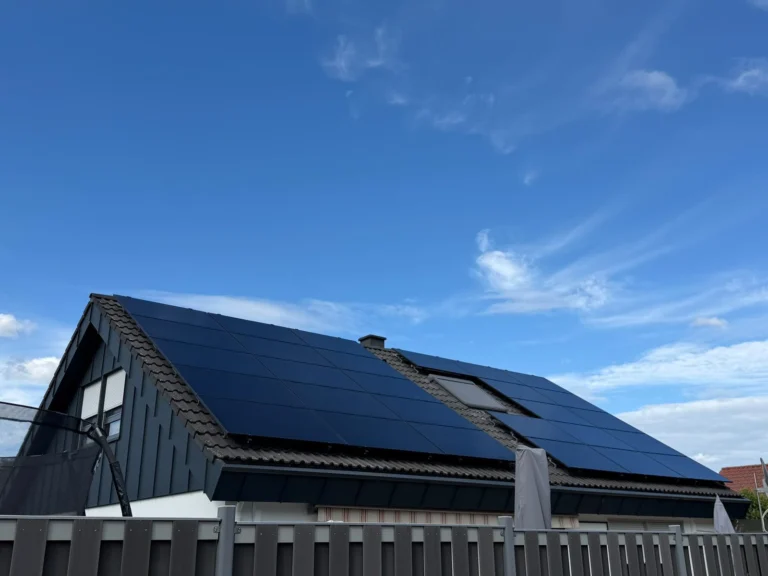 Schwarze Solarmodule auf einem dunklen Satteldach unter blauem Himmel