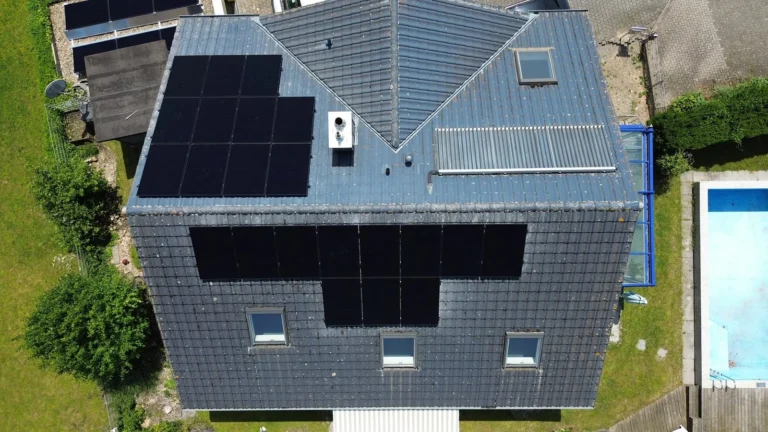 Luftaufnahme: Solarmodule auf einem grauen Dach, daneben ein Pool