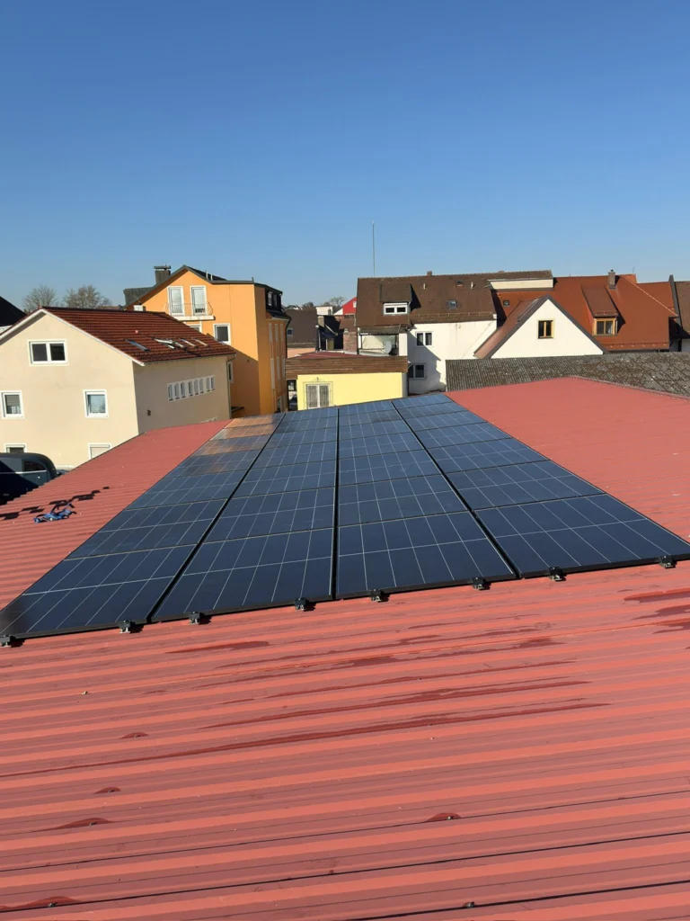Solarmodule auf einem roten Trapezblechdach, dahinter Wohnhäuser