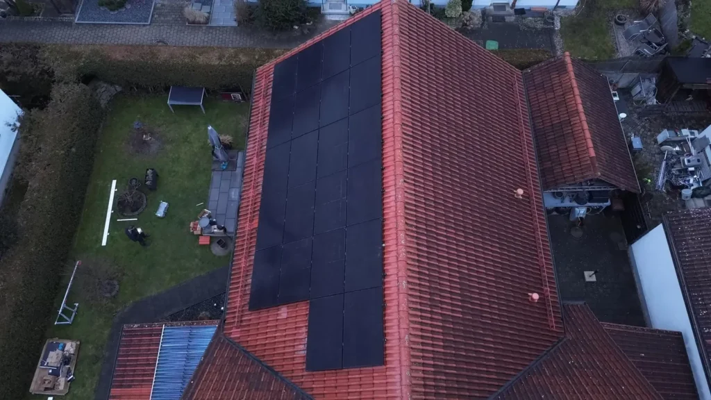 Luftaufnahme: schwarze Solarmodule auf dem roten Ziegeldach eines Wohnhauses mit Garten