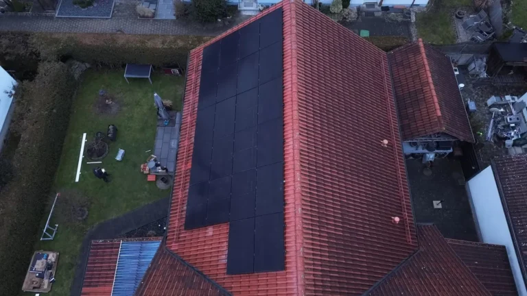 Luftaufnahme: schwarze Solarmodule auf dem roten Ziegeldach eines Wohnhauses mit Garten