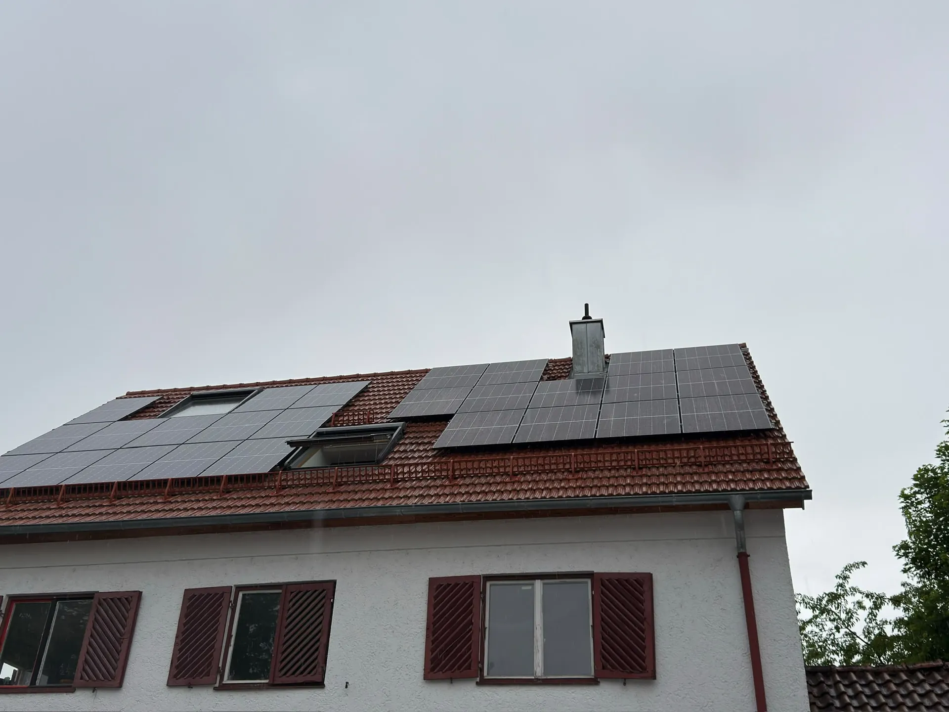 Wohnhaus mit Photovoltaikanlage auf dem roten Ziegeldach und Fensterläden an der Fassade